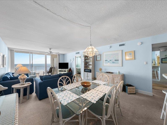 dining space with ceiling fan with notable chandelier, a wall of windows, a textured ceiling, and carpet floors