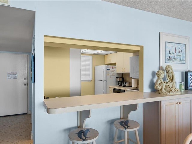 kitchen with white refrigerator, light tile patterned flooring, a breakfast bar, and a textured ceiling