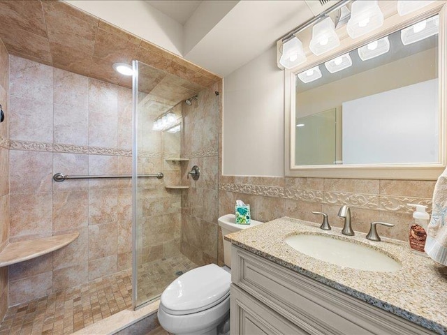 bathroom featuring toilet, tiled shower, decorative backsplash, tile walls, and vanity