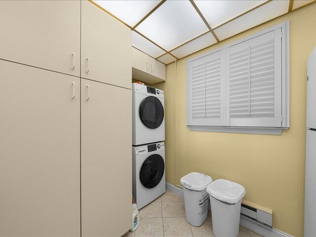 clothes washing area featuring baseboard heating, cabinets, and stacked washer / drying machine