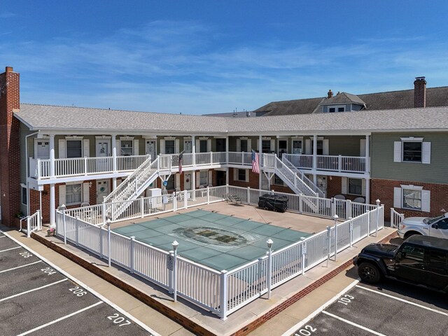 rear view of property with a community pool, uncovered parking, fence, and stairs
