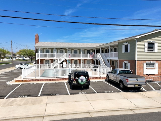 townhome / multi-family property with a chimney, stairs, a porch, and uncovered parking