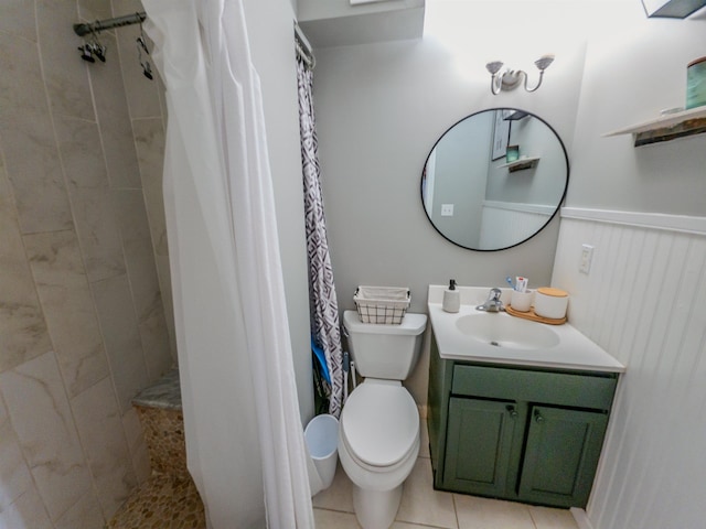 bathroom featuring toilet, tiled shower, tile patterned floors, wainscoting, and vanity