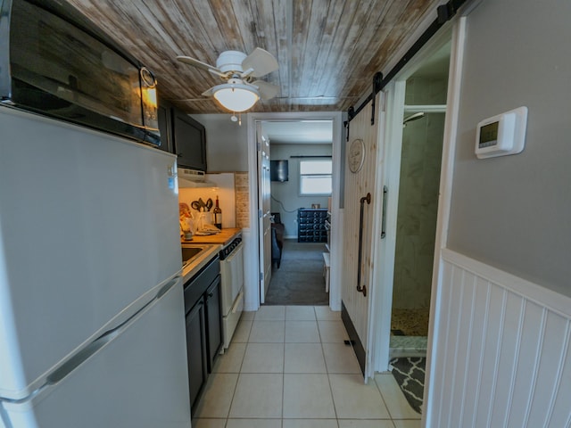 kitchen featuring freestanding refrigerator, light tile patterned flooring, a barn door, a ceiling fan, and dark cabinetry