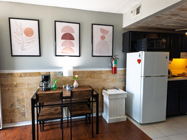 kitchen with freestanding refrigerator, dark cabinetry, visible vents, black microwave, and a wainscoted wall
