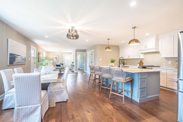 kitchen with a kitchen island with sink, sink, white cabinetry, hanging light fixtures, and a breakfast bar area