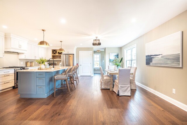 kitchen featuring stainless steel appliances, a kitchen breakfast bar, pendant lighting, a center island with sink, and white cabinets