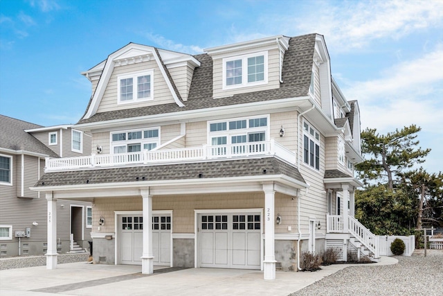 shingle-style home with an attached garage, a balcony, a gambrel roof, driveway, and roof with shingles