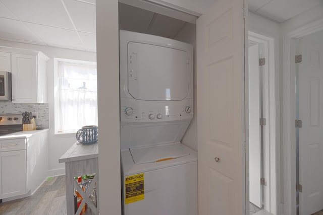 washroom with baseboards, light wood finished floors, laundry area, and stacked washer / dryer