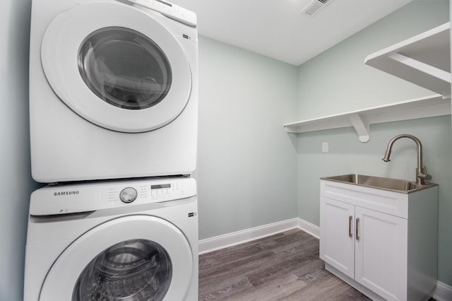 laundry area featuring cabinets, wood-type flooring, stacked washing maching and dryer, and sink