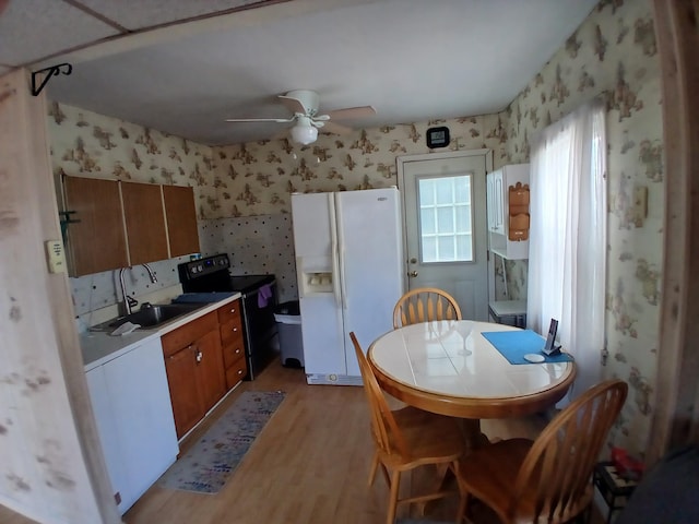 kitchen with a sink, range with electric cooktop, wallpapered walls, and white fridge with ice dispenser