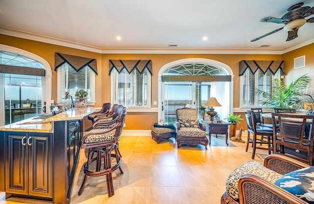 interior space with ornamental molding, light stone countertops, plenty of natural light, and a breakfast bar area