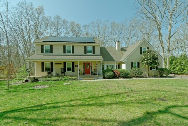 view of front of property featuring a chimney, a porch, a front lawn, and roof mounted solar panels