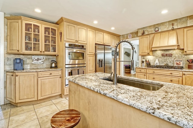 kitchen featuring light brown cabinets, custom exhaust hood, tasteful backsplash, a sink, and appliances with stainless steel finishes