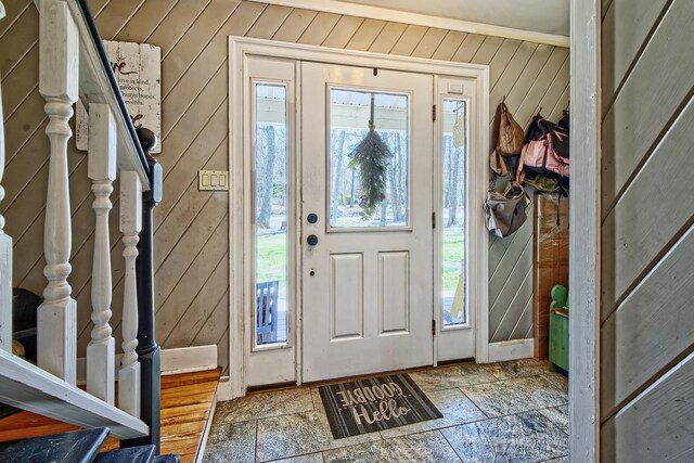 entrance foyer featuring stairs, wood walls, and stone tile flooring
