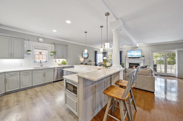 kitchen with a sink, stainless steel appliances, gray cabinetry, a kitchen bar, and backsplash