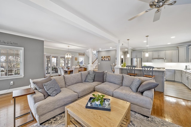 living area featuring light wood finished floors, baseboards, stairs, crown molding, and ornate columns