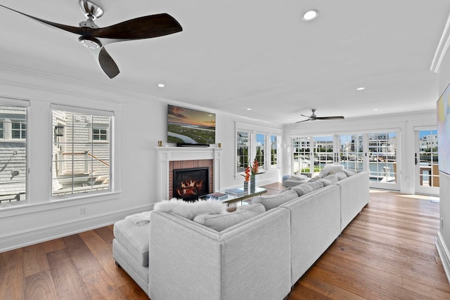 living room featuring ceiling fan, a fireplace, hardwood / wood-style floors, and ornamental molding