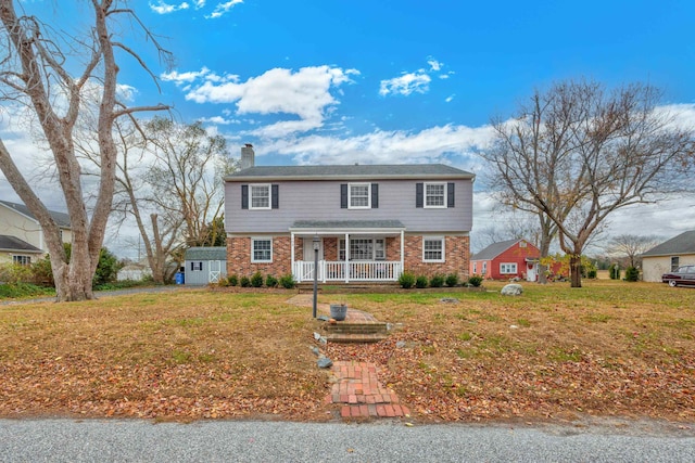 view of front of home featuring covered porch, a front lawn, and a storage shed