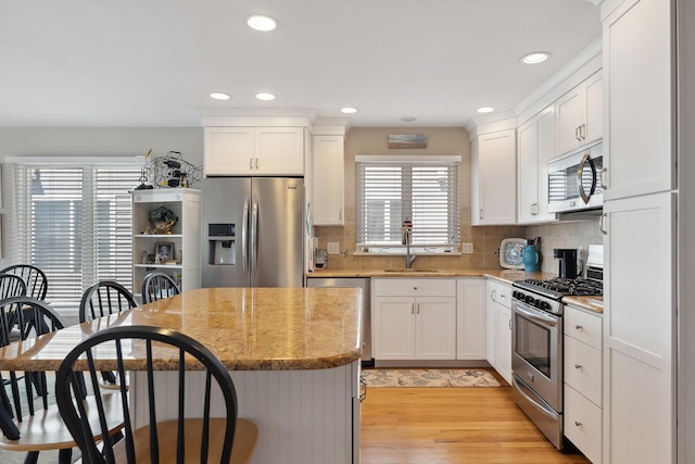 kitchen with a kitchen island, appliances with stainless steel finishes, a breakfast bar area, white cabinetry, and a sink