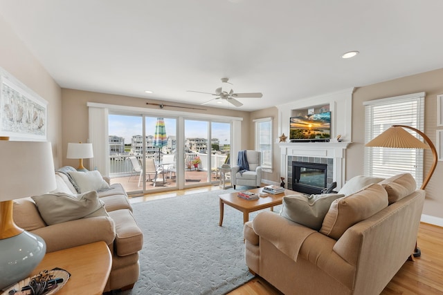 living room with a tile fireplace, recessed lighting, a ceiling fan, baseboards, and light wood-style floors