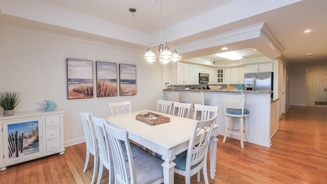 dining room with ornamental molding, light hardwood / wood-style floors, a raised ceiling, and a chandelier