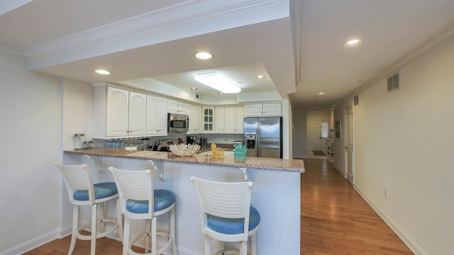 kitchen with hardwood / wood-style flooring, white cabinetry, stainless steel appliances, light stone countertops, and kitchen peninsula