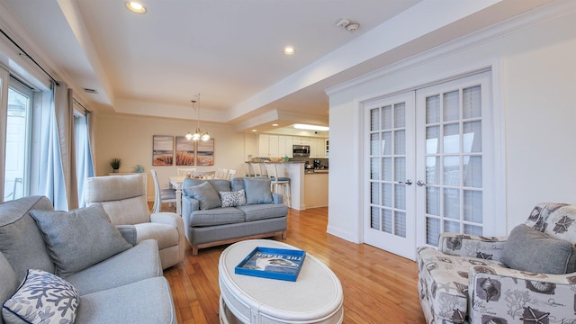 living room featuring a tray ceiling, a notable chandelier, light hardwood / wood-style floors, and french doors