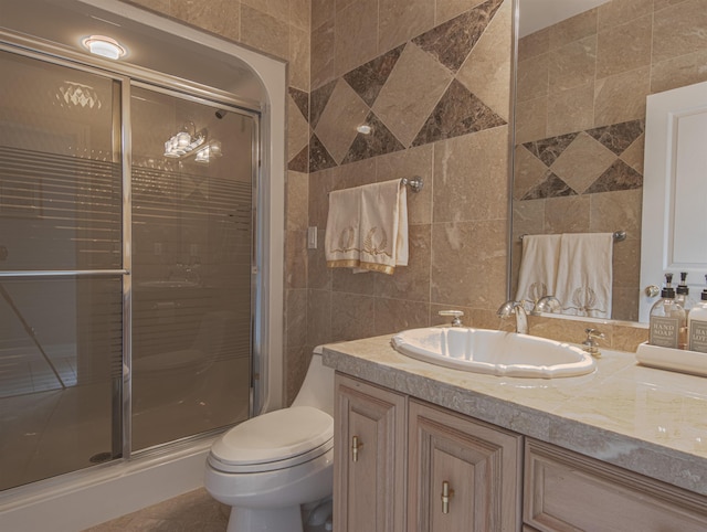 bathroom with vanity, toilet, a shower with shower door, and tile walls