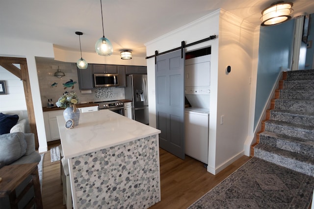 kitchen with hardwood / wood-style flooring, hanging light fixtures, stainless steel appliances, a barn door, and stacked washer / dryer