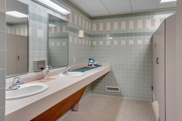 bathroom with tile patterned flooring, a paneled ceiling, tile walls, and vanity