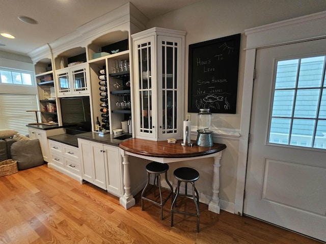 bar featuring white cabinets, ornamental molding, and light wood-type flooring