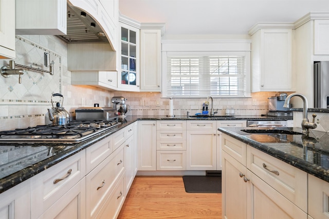 kitchen with dark stone countertops, sink, stainless steel appliances, and light hardwood / wood-style flooring