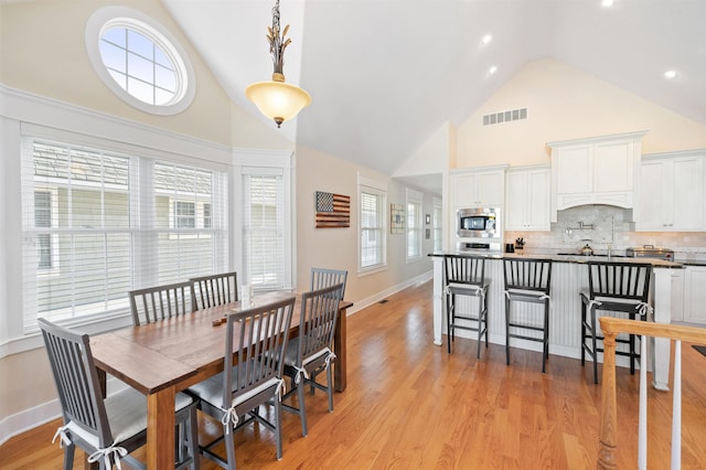 dining space featuring a wealth of natural light, high vaulted ceiling, and light wood-type flooring