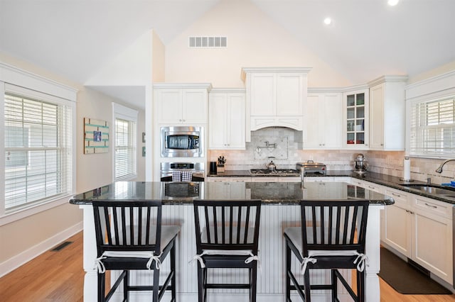 kitchen featuring a kitchen island with sink, stainless steel microwave, dark stone counters, and sink