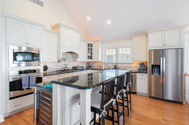 kitchen with tasteful backsplash, dark stone counters, stainless steel appliances, a center island with sink, and wine cooler