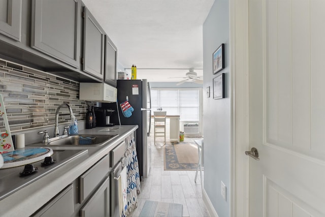 kitchen with decorative backsplash, gray cabinetry, ceiling fan, sink, and stovetop