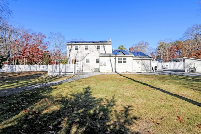 rear view of house with roof mounted solar panels, a fenced backyard, and a yard