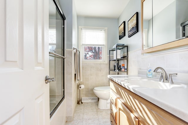 bathroom featuring toilet, a wainscoted wall, shower / bath combination with glass door, vanity, and tile patterned floors