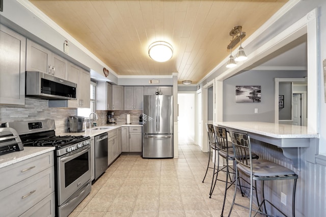 kitchen with a breakfast bar area, stainless steel appliances, a sink, gray cabinets, and backsplash