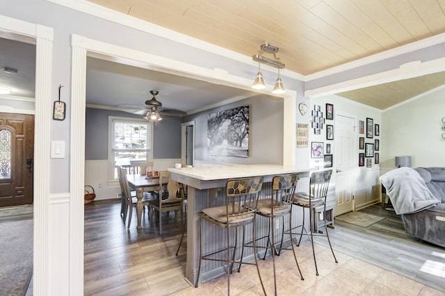 bar with a wainscoted wall, crown molding, light wood-style flooring, and pendant lighting