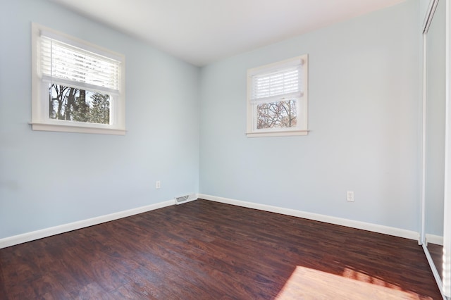 unfurnished room featuring baseboards, dark wood finished floors, and a wealth of natural light