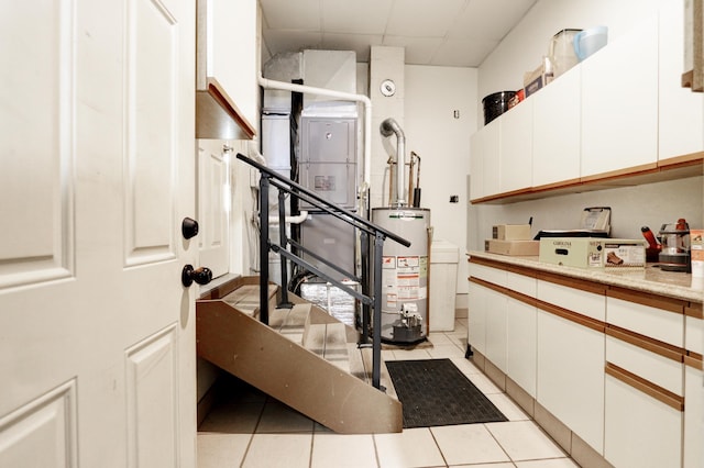 interior space featuring light countertops, water heater, light tile patterned flooring, white cabinets, and a drop ceiling