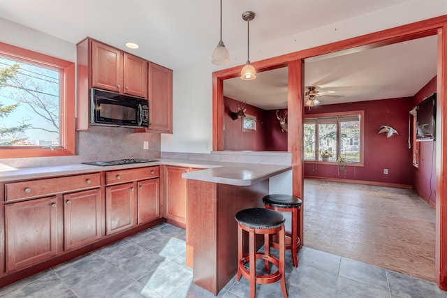 kitchen with black microwave, light countertops, brown cabinets, a kitchen bar, and stovetop