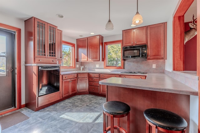 kitchen with glass insert cabinets, dishwashing machine, black microwave, a kitchen bar, and a peninsula