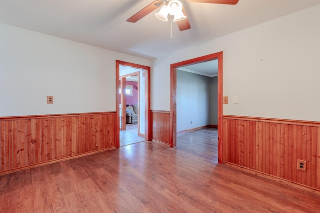 spare room featuring wooden walls, wainscoting, a ceiling fan, and wood finished floors