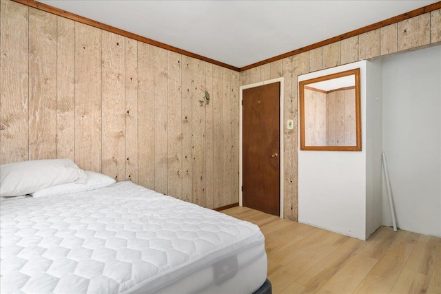 bedroom featuring wood walls, light hardwood / wood-style floors, ornamental molding, and a closet