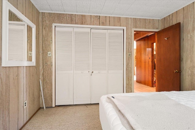 carpeted bedroom featuring wooden walls, a closet, and crown molding