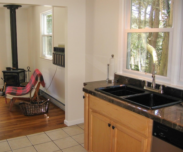 kitchen with stainless steel dishwasher, a wood stove, sink, and light tile patterned floors