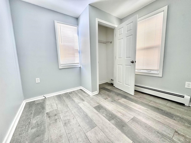 unfurnished bedroom with a baseboard heating unit, a closet, and light wood-type flooring